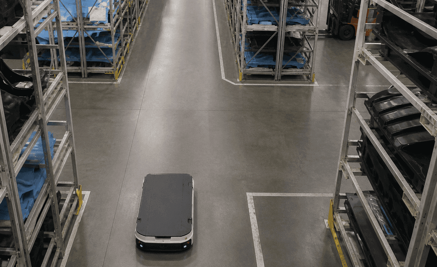 A forklift and an AMR maintaining a safe distance at an intersection hidden by high parts racks